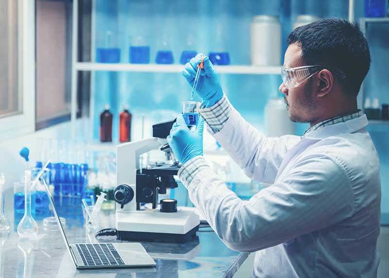 Homem cientista aplicando um produto químico através de um conta-gotas em um becker químico dentro de um laboratório