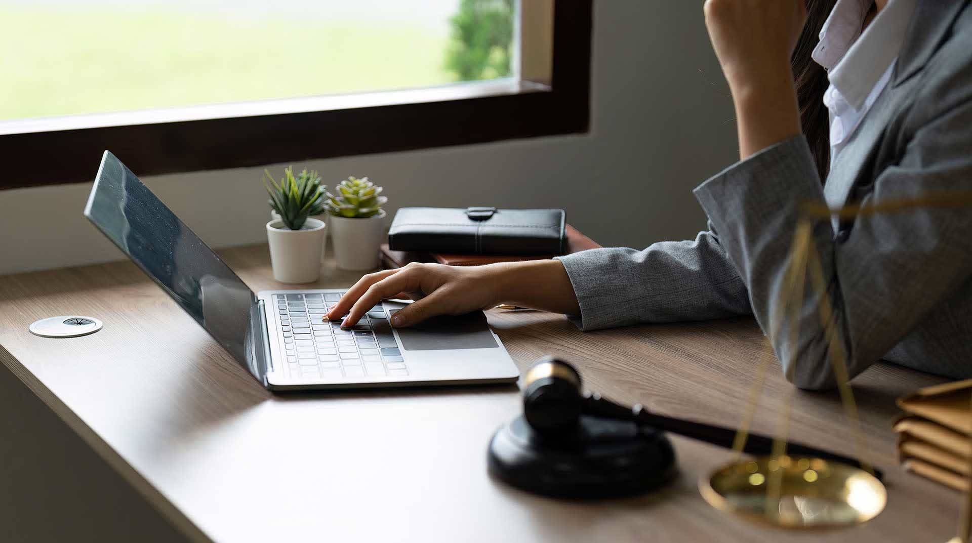 Mulher digitando em um laptop sob uma mesa de madeira em um escritório corporativo